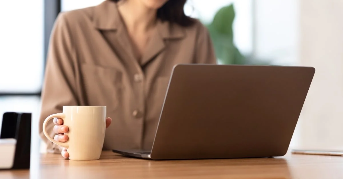 Femme qui tient une tasse de café devant son ordinateur portable